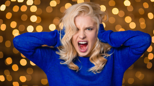 Woman with hands over ears and screaming with holiday lights behind her.