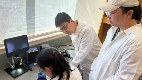 Three scientists in white lab coats in electronics lab