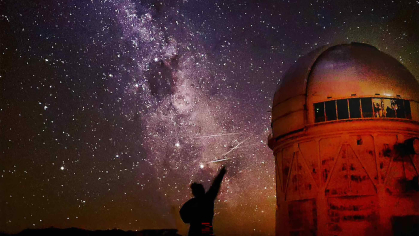 Person silhouetted against the sky with stars above and an observatory to the right