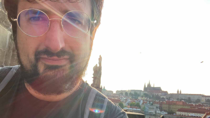 Ilya Slavutskiy stands near Charles Bridge. Behind him is a view of the Prague Castle complex and St. Vitus Cathedral.