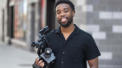 Terrance Leon George III standing in front of the Mason Gross building with his camera in his hand