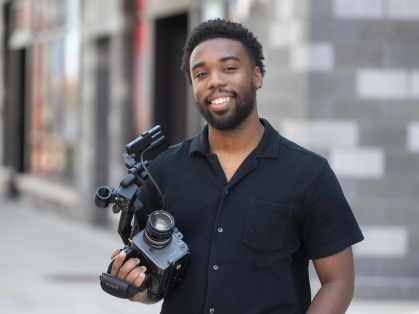 Terrance Leon George III standing in front of the Mason Gross building with his camera in his hand