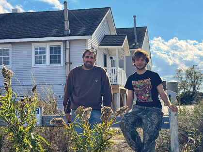 Two men posing in front of a large building on the beach.