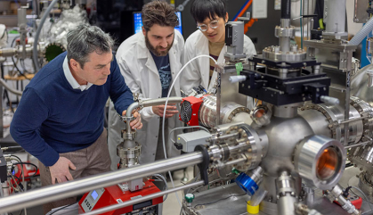 Three scientists in white lab coats in electronics lab