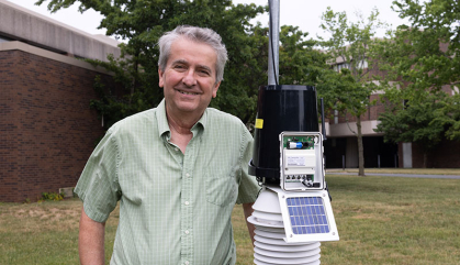 Man in a green shirt standing next to weather equipment. He is outside.