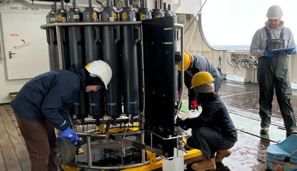 A group of people in hardhats on a sea vessel adjusting a piece of lab machinery