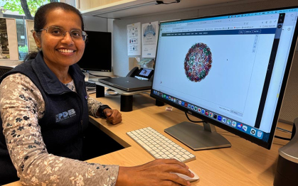 Woman in a blue vest sits before a computer screen with a protein structure on the screen