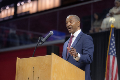 Rutgers President William F. Tate IV is shown behind a podium withe American flag in the background