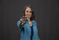 Woman in light blue sweater holds up breccia, a type of rock found on the Moon.